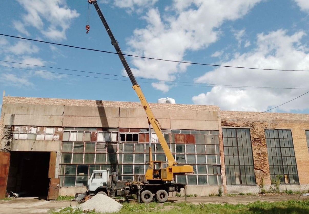 Автокран с поднятой стрелой у производственного корпуса