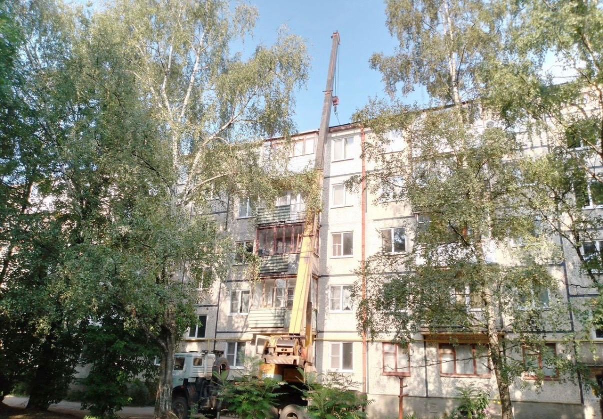 Автокран во дворе пятиэтажного дома со стрелой, поднятой на уровень кровли